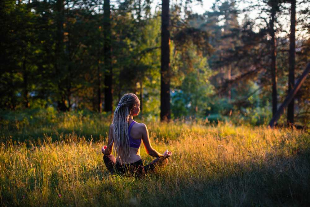 Woman meditating outdoors in a sunlit forest clearing, embodying mindfulness and self-care in nature